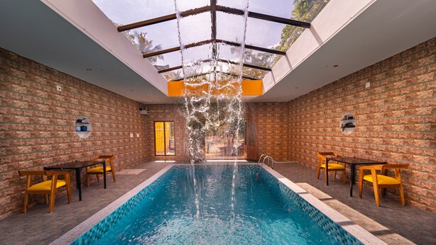 Une piscine agrémentée d’une cascade, entourée de murs en briques et de chaises en bois.