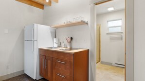 A compact kitchen with a white refrigerator, wooden cabinets, a countertop, and a wooden shelf above the sink.
