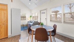 A modern living room with a dining area, a ceiling fan, and large windows.