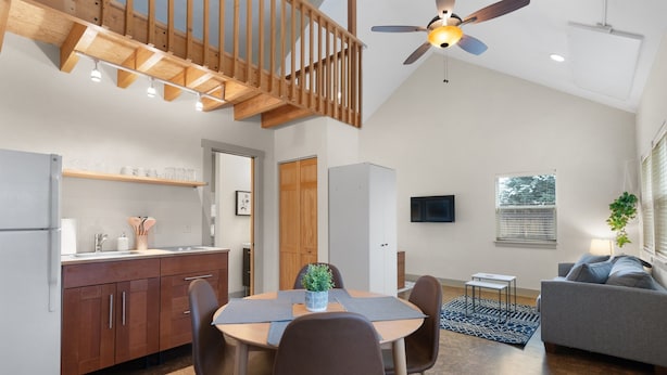 A modern kitchen with wooden cabinets, a dining table with chairs, a ceiling fan, and a large window.