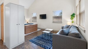 A modern living room with a high ceiling, a white wardrobe, a grey sofa, a small white table, and a blue patterned rug.