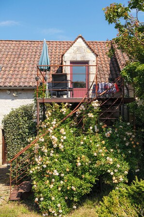 A rustic house with a tiled roof, a balcony with a chair and table, and a rose bush in the foreground. - Chambre Lucy 2 Adults, salted heated swimming pool (june to septembre) , spa (Ajat)