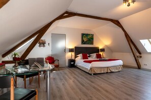 A bedroom with a sloped ceiling, a bed with red and white bedding, a desk with a chair, and a painting on the wall.