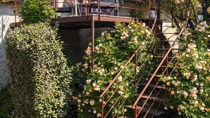 Eine rustikale Treppe führt zu einem Haus mit Ziegeldach, umgeben von üppigem Grün und blühenden Blumen.