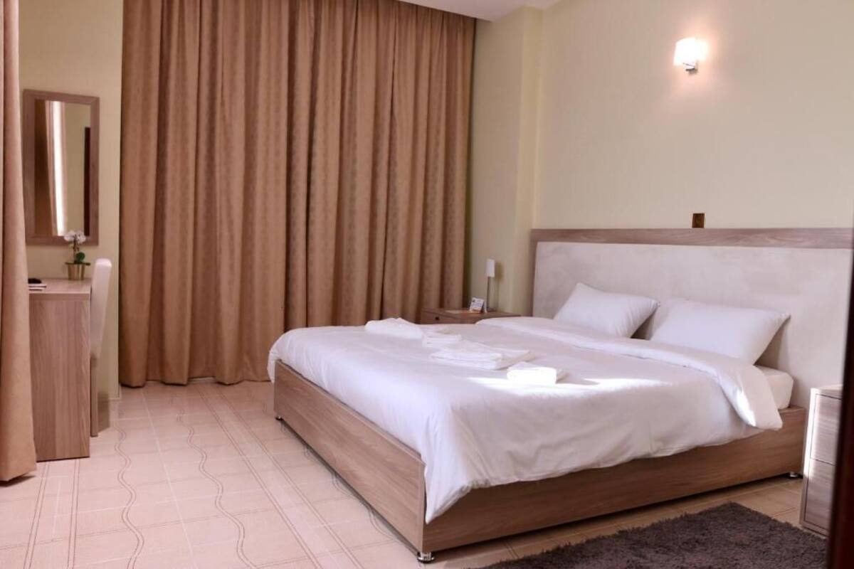 A neatly made bed with white linens, a wooden headboard, and a nightstand with a lamp.