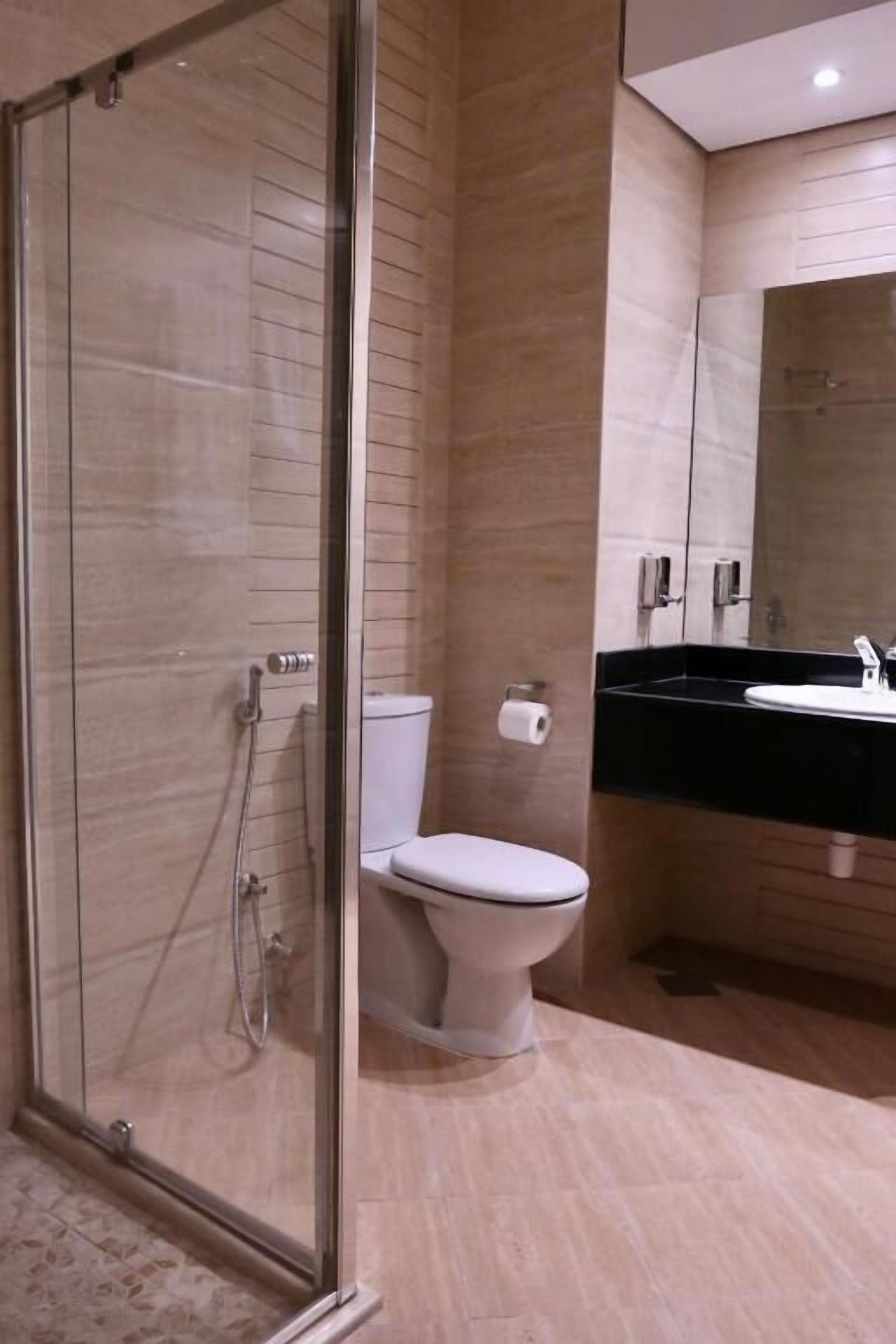 Un baño moderno con cabina de ducha de vidrio, un inodoro y un lavabo sobre encimera negra.