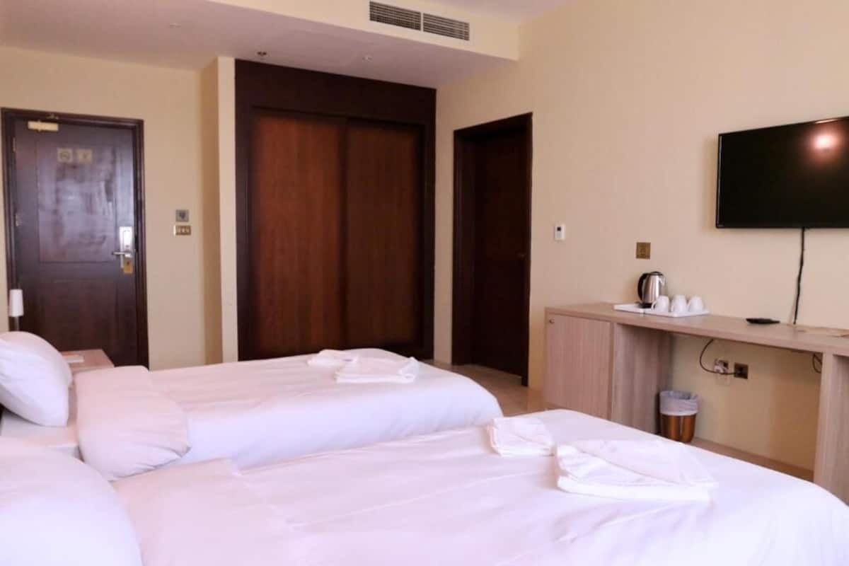 A hotel room with two beds, a TV, a desk with a coffee maker, and a trash can.