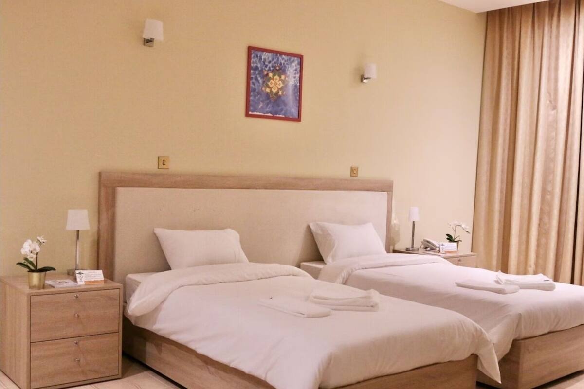 A hotel room with two beds, a nightstand with a lamp, a small table with a phone, and a painting on the wall.