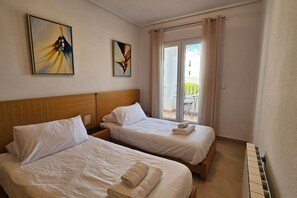 Ein Hotelzimmer mit zwei Betten, einem Holzkopfstück, einem Balkon mit Blick und zwei gerahmten Kunstwerken an der Wand.