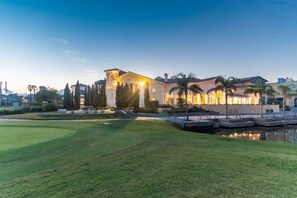 Ein gepflegter Golfplatz mit Clubhaus, Palmen und einem ruhigen Wasserspiel.