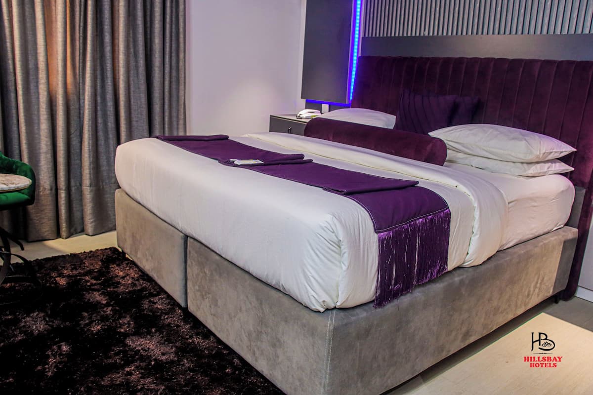 A modern bedroom with a large bed, a nightstand, and a green chair.