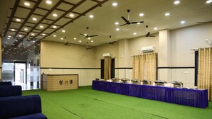 A conference room with green carpet, blue sofas, a long table with food service, ceiling fans, and an air conditioning unit. - Hotel Crown Royal (Kota)