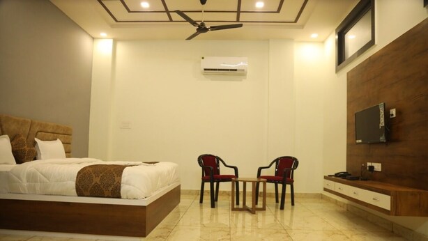 A hotel room with a bed, two chairs, a small table, a TV, and an air conditioning unit. - Hotel Crown Royal (Kota)