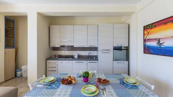A dining area with a table set for four, a kitchen in the background, and a painting on the wall.