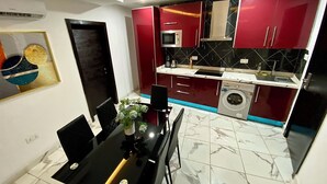Une cuisine compacte avec des meubles rouges, un four à micro-ondes encastré et un lave-linge.