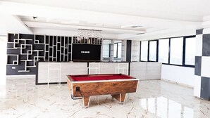 Une table de billard moderne, installée dans un espace intérieur spacieux, agrémentée d’un mur au motif géométrique, d’une grande fenêtre et d’un lustre.