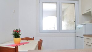 Ein kleiner, sauberer Raum mit einem Tisch, einem Stuhl, einem Fenster und einer Küchenzeile.
