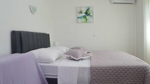 Ein Schlafzimmer mit Bett, Kissen, Decke, einer Wand-Klimaanlage und einem Gemälde.
