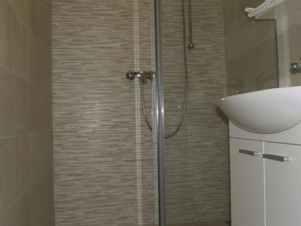 A bathroom with a glass shower enclosure, a white sink, and a tiled wall.
