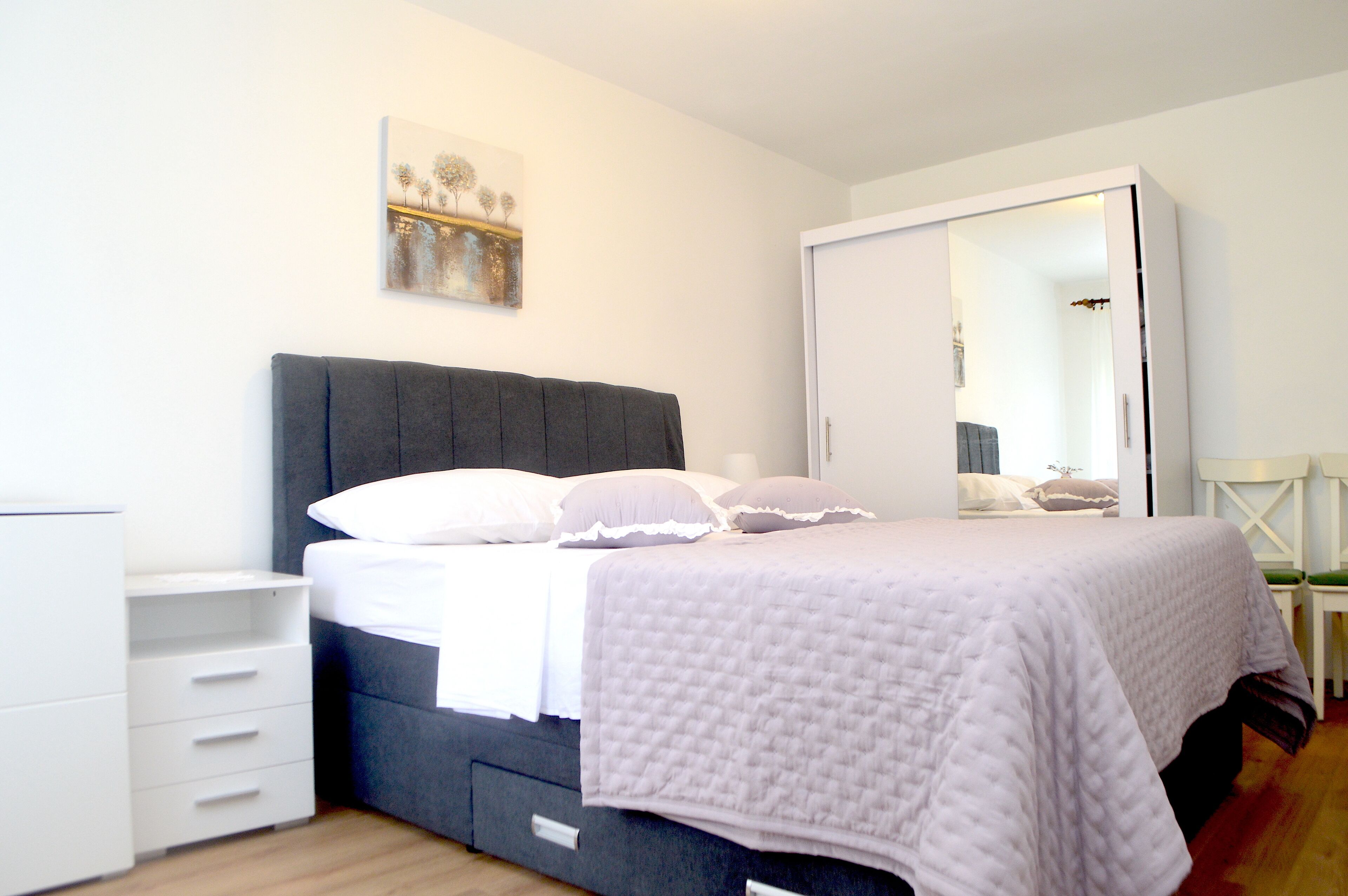 Ein Schlafzimmer mit einem Bett, einem Kleiderschrank, einem Nachttisch und einem an der Wand befestigten Kunstwerk.
