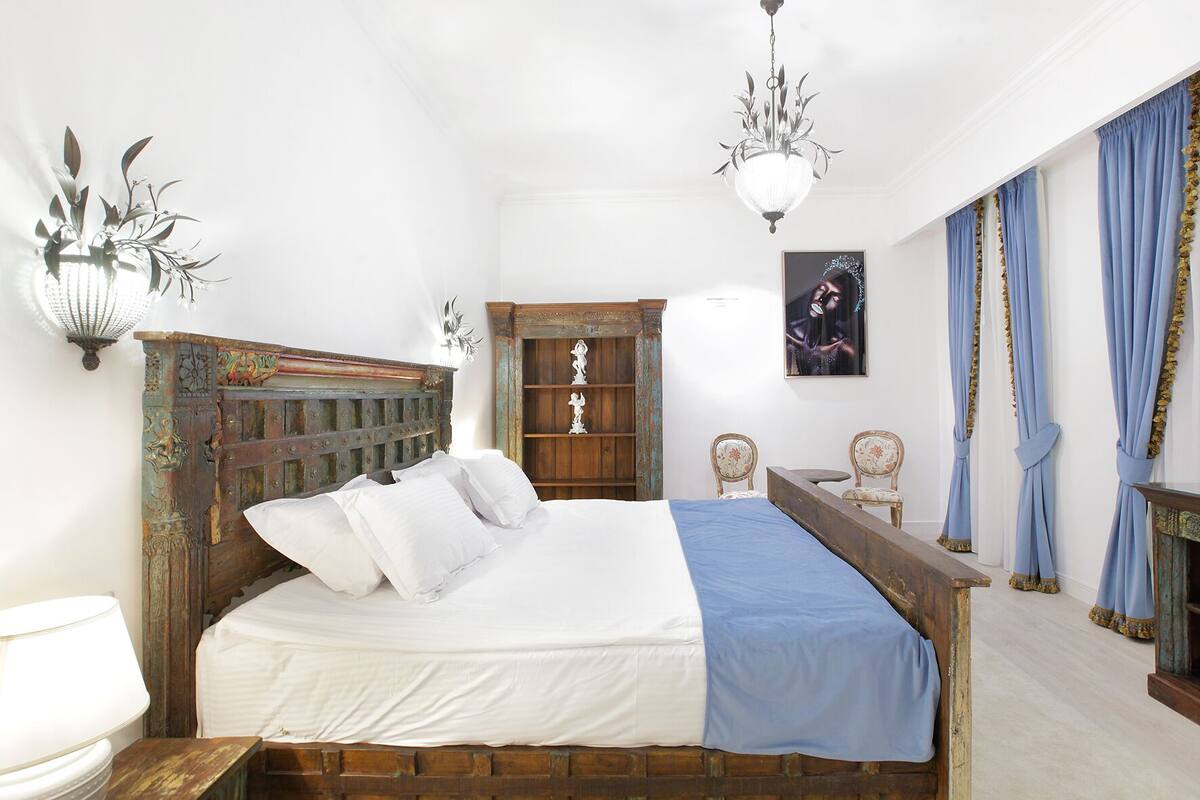 Een slaapkamer met een houten bed, nachtkastje, kapstok en een kroonluchter.
