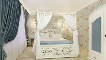 Una cama con dosel y cuatro columnas, con un fondo de papel tapiz floral, un armario blanco y una mesita de noche pequeña.