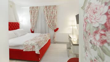 A bedroom with a red bed, white curtains, a bedside table with a lamp, and a red chair.
