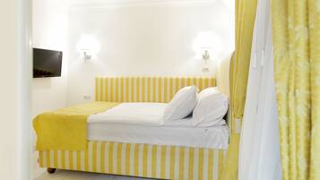 A bed with yellow and white striped bedding, a flat-screen TV on the wall, and a yellow curtain.
