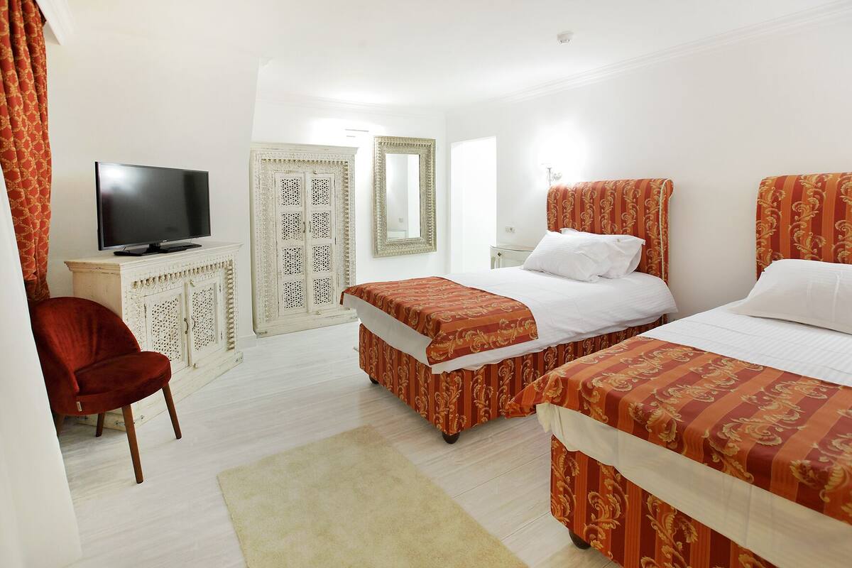 Een hotelkamer met twee bedden, een televisie, een kledingkast en een rode stoel.