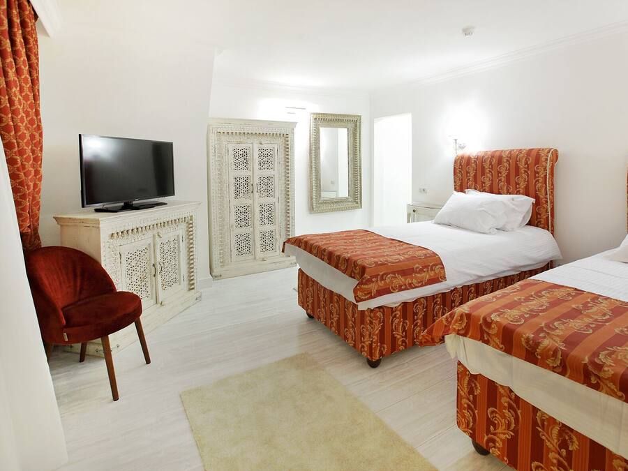 A hotel room with two beds, a television, a wardrobe, and a red chair.