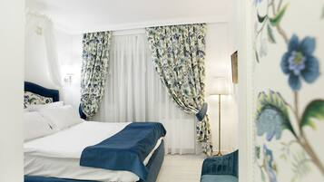 A hotel room with a bed, a chair, a lamp, and floral curtains.
