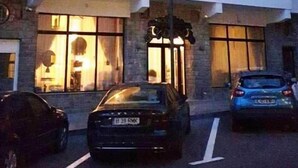 Un immeuble à plusieurs étages, doté d’une façade blanche imposante et d’un toit sombre. Plusieurs fenêtres laissent entrevoir une lumière intérieure chaleureuse, et une voiture est garée devant.