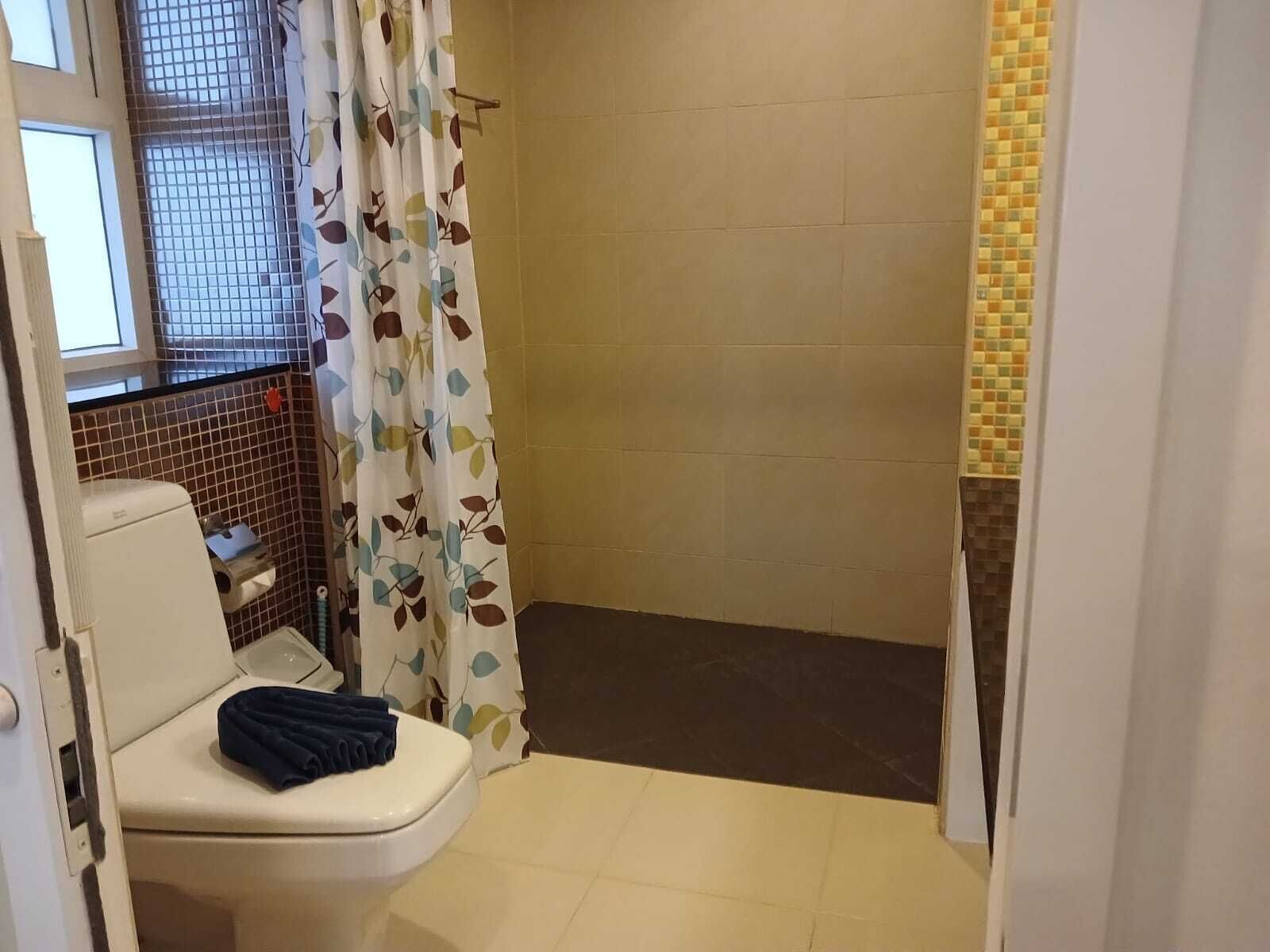 Ein kleines Badezimmer mit Toilette, einer Dusche mit einem Duschvorhang mit Blattmuster und gefliesten Wänden.