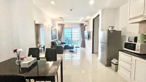 A modern hotel room with a dining area, a living room with a sofa and TV, and a kitchenette.