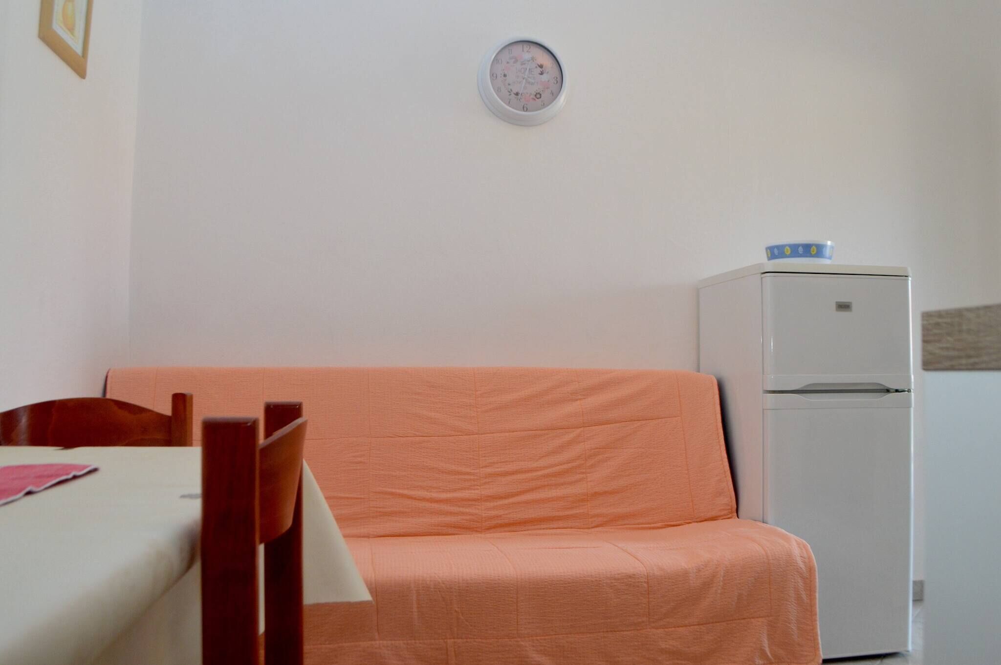 A room with a bed, a table, a chair, a sofa, and a refrigerator.