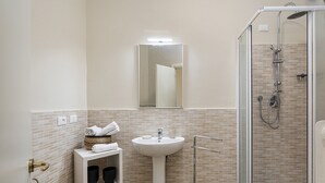 A bathroom with a white sink, a mirror, a shower enclosure, and a shelf with towels and toiletries. - Sea View Flat in Rapallo by Wonderful Italy (Rapallo)