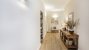 A hallway with a wooden floor, a bench, a table with a vase, and wall-mounted artwork. - Sea View Flat in Rapallo by Wonderful Italy (Rapallo)