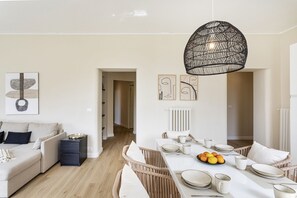 Ein modernes Wohnzimmer mit Essbereich, ausgestattet mit einem großen Esstisch für vier Personen, einer Couch und einer hängenden Leuchte.