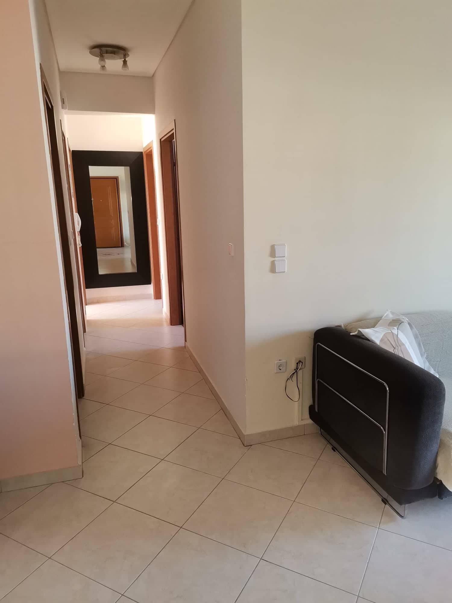 Un pasillo con una cama y una mesita de noche, que conduce a una habitación con una puerta al final.