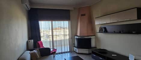 A living room with a sofa, a TV, a fireplace, and a balcony with a view.