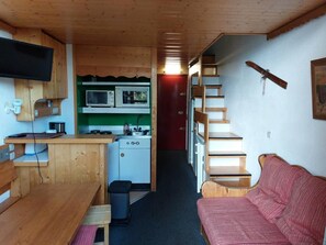 A compact kitchen with a microwave, stove, and sink. There is a wooden bench and a small trash bin. A red door leads to another room. - 50m from ski slopes, Ground floor, balcony, tv, 30m², Les Arcs (Les Arcs)