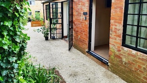 A brick building with a gravel courtyard, a door leading to a room, and a sign indicating "Room 1." - Cotswold Bankview (Moreton-in-Marsh)