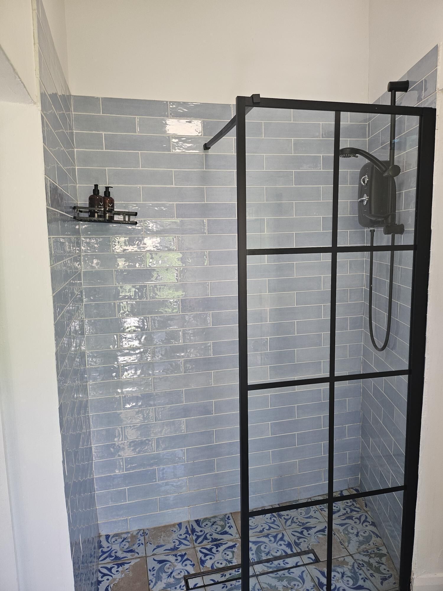 A shower area with a glass door, tiled walls, and a shelf with toiletries.
