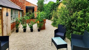 A courtyard with a brick building, potted plants, and outdoor furniture. - Cotswold Bankview (Moreton-in-Marsh)