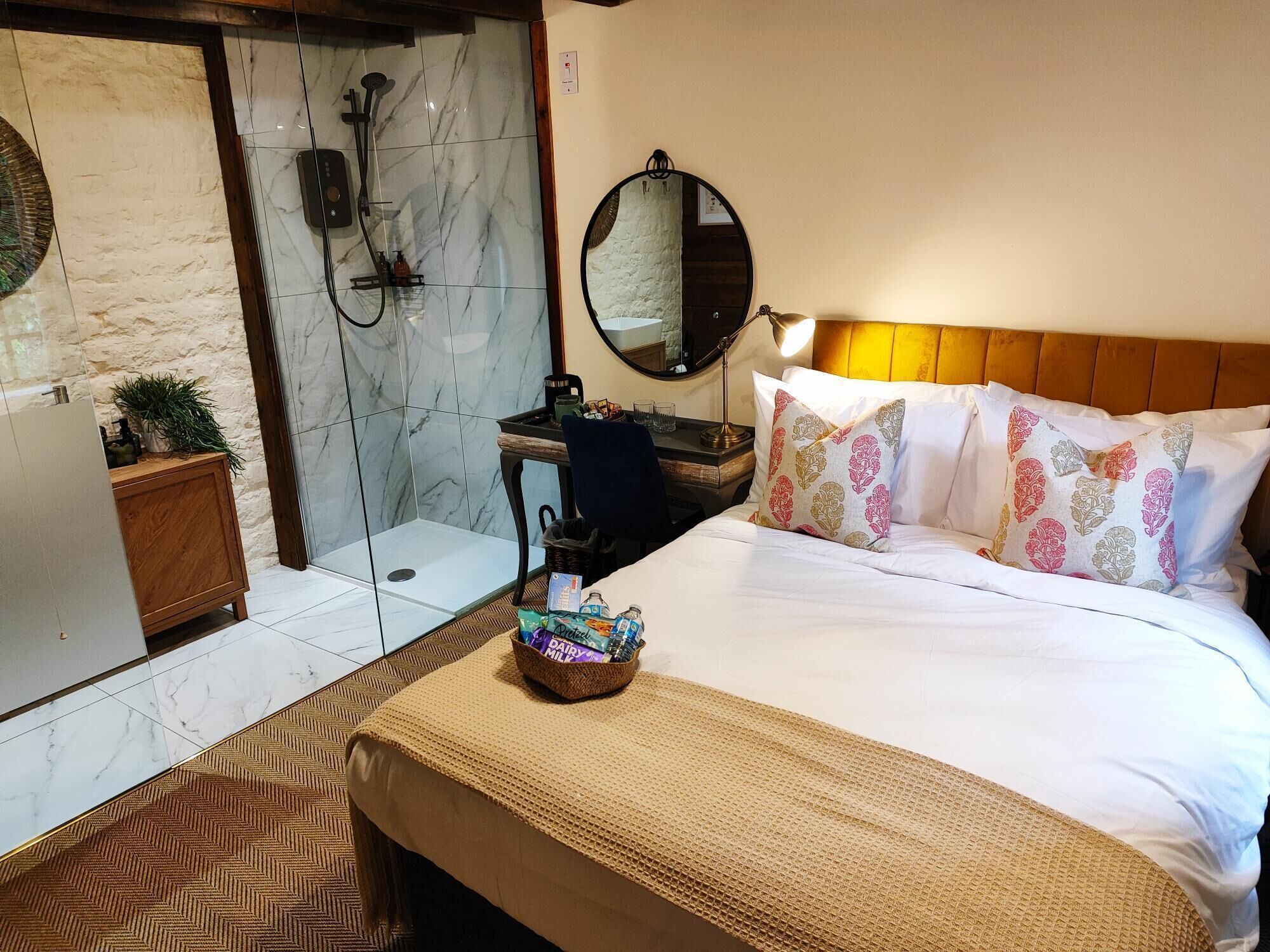 A hotel room with a bed, a bedside table, a mirror, a shower area, and a small wooden cabinet.