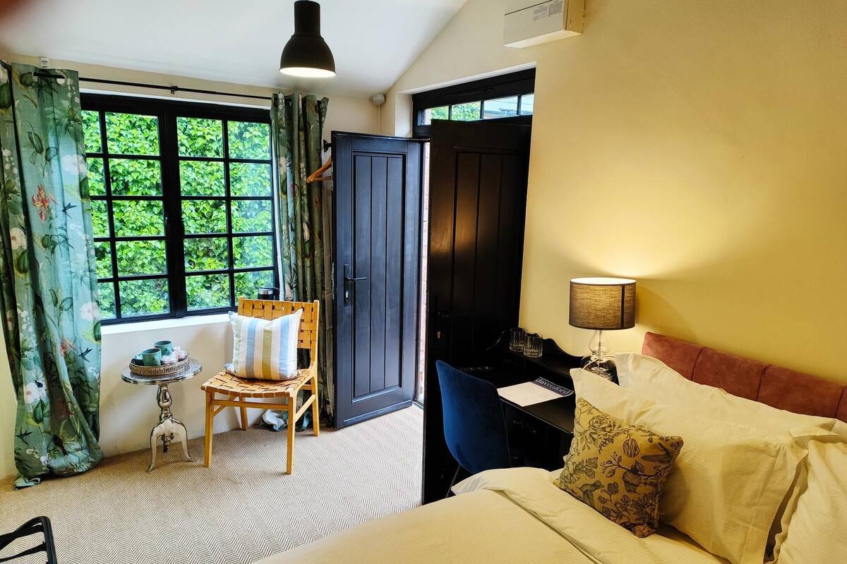 A hotel room with a bed, a desk, a chair, a table with a tray, and a window with curtains.