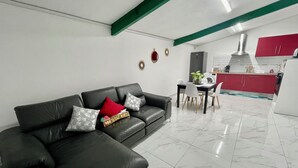 Een moderne woonkamer met een zwarte leren bank, een eettafel met stoelen, een keuken met rode kasten en een vloer van witte tegels.