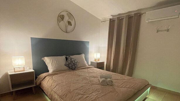 Een slaapkamer met een bed, nachtkastjes, een ventilator aan de muur en een gordijn.