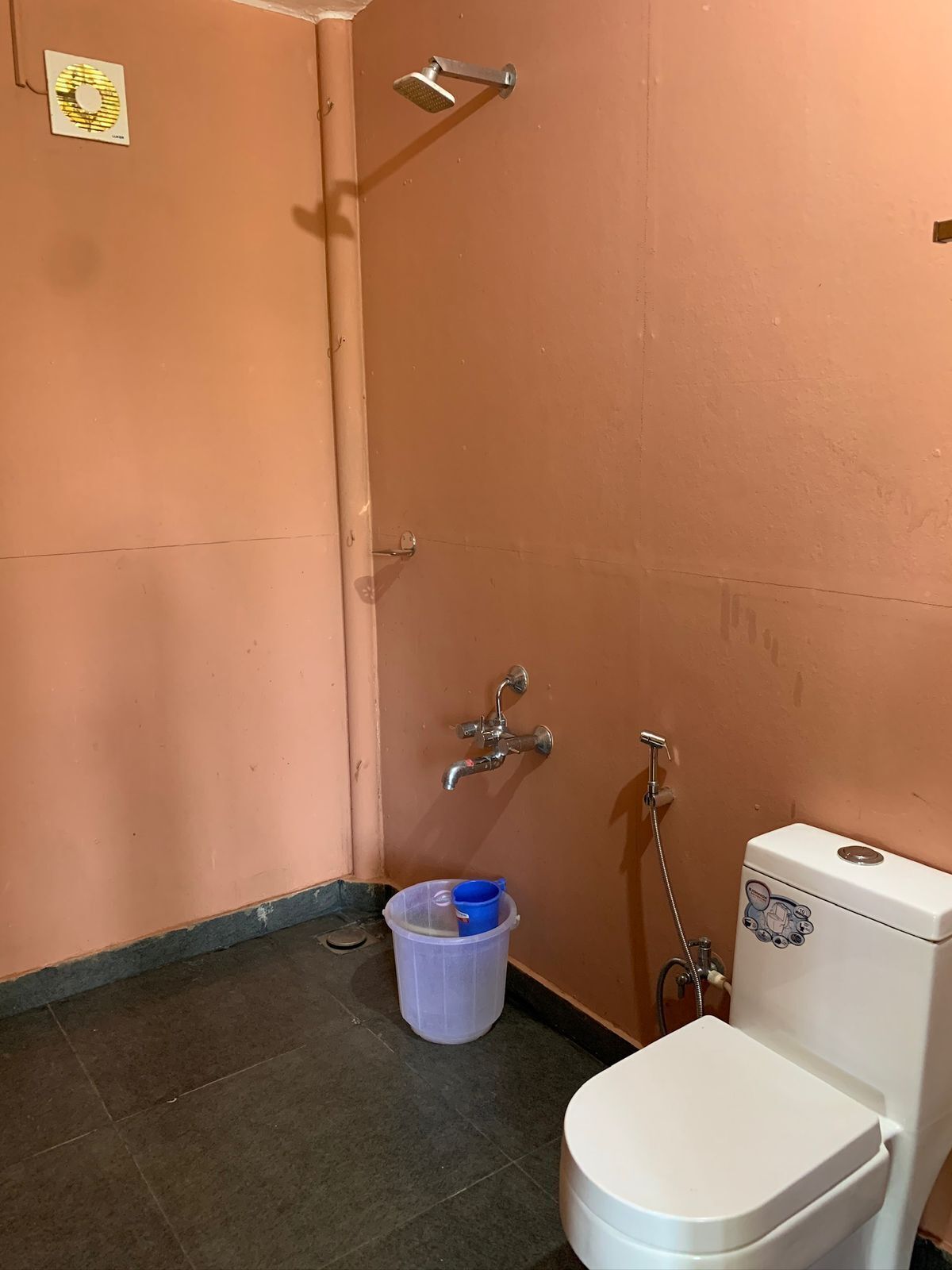 A small bathroom with a toilet, a shower, and a plastic container on the floor.