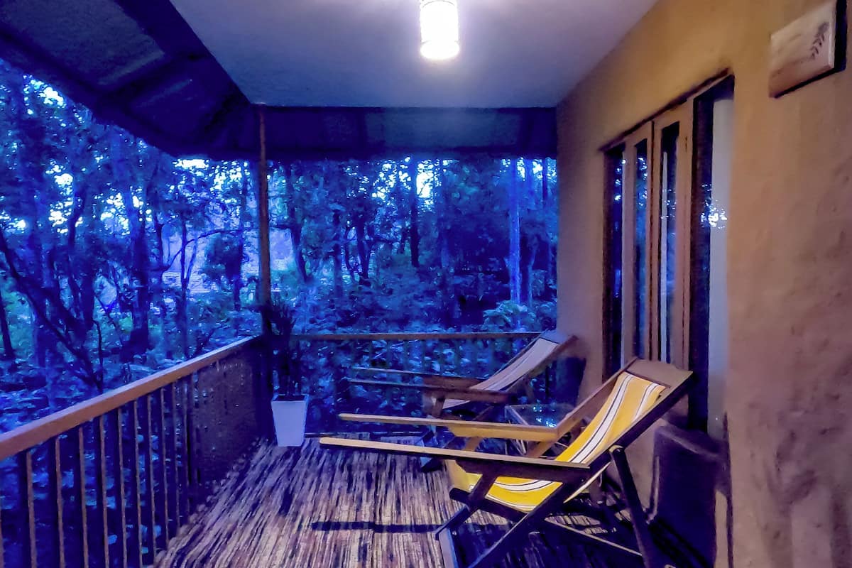 Un balcon doté d’un plancher en bois et de deux fauteuils confortables, donnant sur une zone boisée.